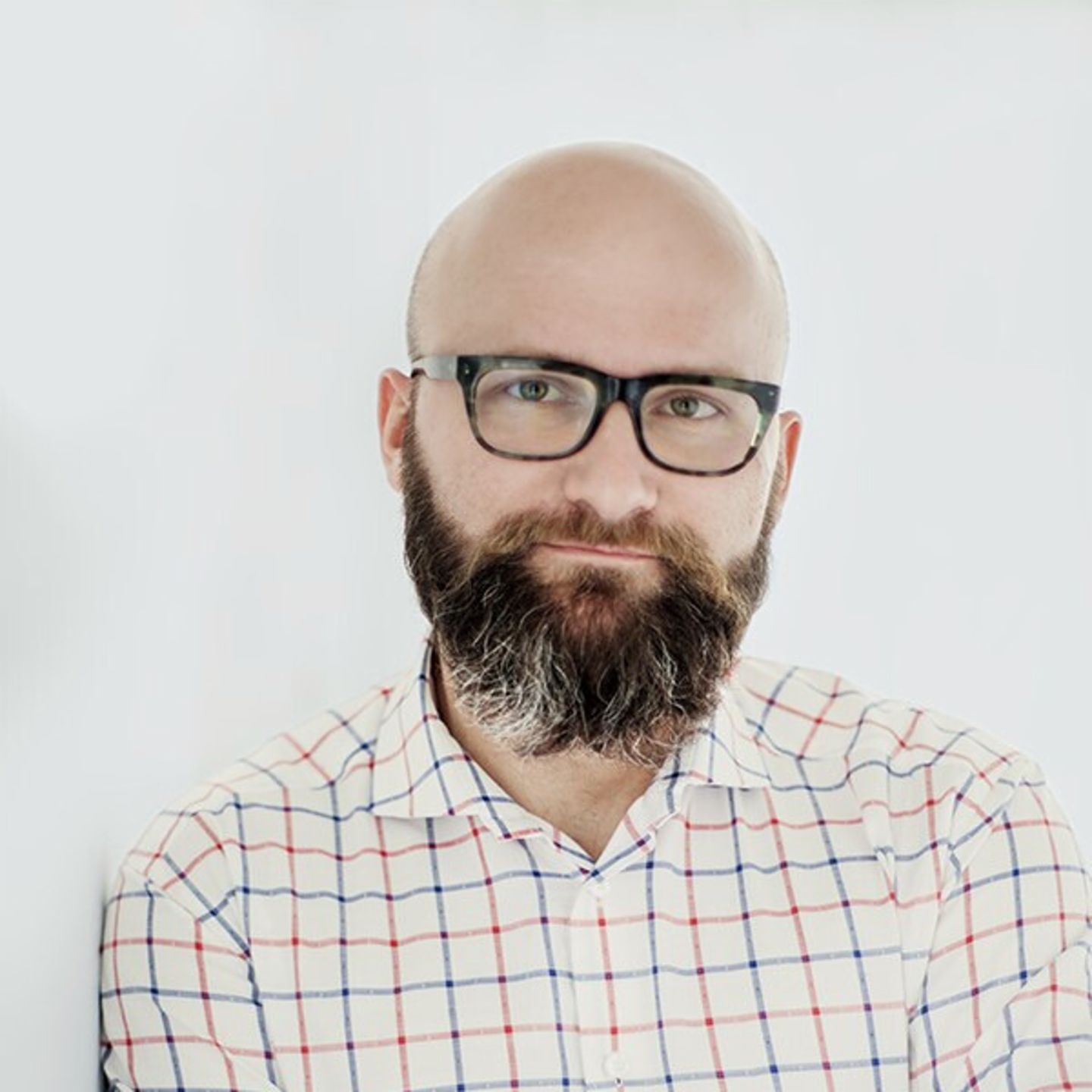 Dr. hab. Tomasz Piekot u košulji na karirane uzorke naslonjen na bijeli zid.