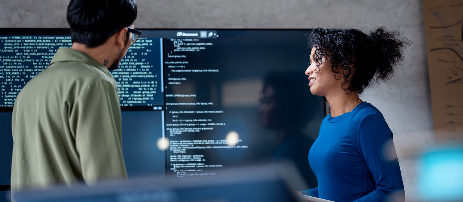 AI u naplati dugova: Na ovoj slici, dva stručnjaka zajednički analiziraju programski kod za automatizovane procese na velikom ekranu. Scena ilustruje praktičnu primenu veštačke inteligencije (AI) i robotizovane automatizacije procesa (RPA) u upravljanju dugovima – primer digitalne transformacije u upravljanju potraživanjima.