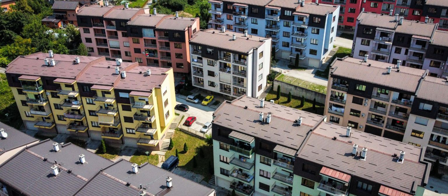 An aerial view highlights a vibrant residential complex featuring numerous multi-colored apartment buildings amidst green surroundings in Bosnia.